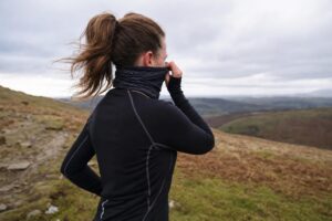 A runner pulling a buff up over their mouth and nose on a windswept winter trail