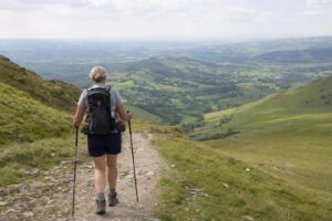 A hiker's hand reaching into a rucksack hip-belt pocket for a small skincare tin on a UK hillside trail