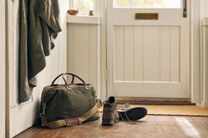 A small weekend bag packed by a front door with walking boots nearby, ready for a spontaneous trip
