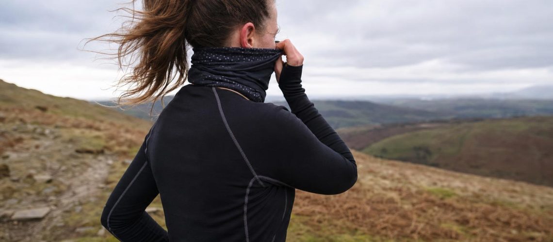 A runner pulling a buff up over their mouth and nose on a windswept winter trail