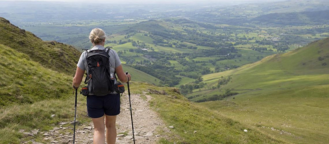 A hiker's hand reaching into a rucksack hip-belt pocket for a small skincare tin on a UK hillside trail