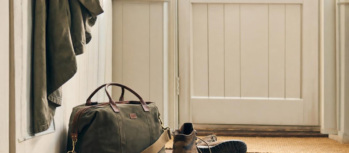 A small weekend bag packed by a front door with walking boots nearby, ready for a spontaneous trip